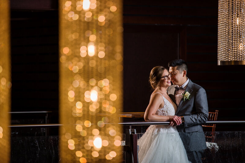 Bride and groom holding each other upstairs at the Phoenixville Foundry, surrounded by modern chandeliers.