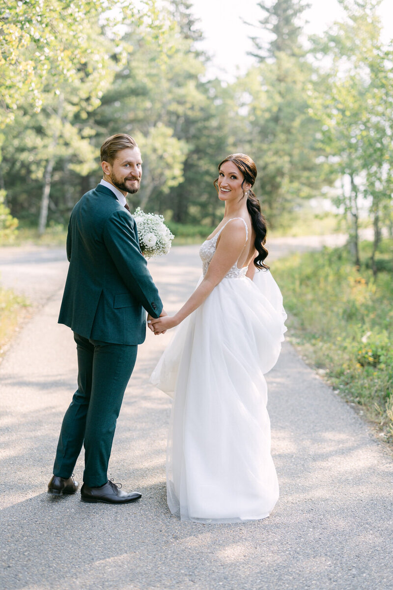 Capture the heartwarming moment of a bride and groom holding hands and smiling as they walk towards Pomeroy Kananaskis Lodge after their first look. A perfect blend of love and joy in a stunning setting.