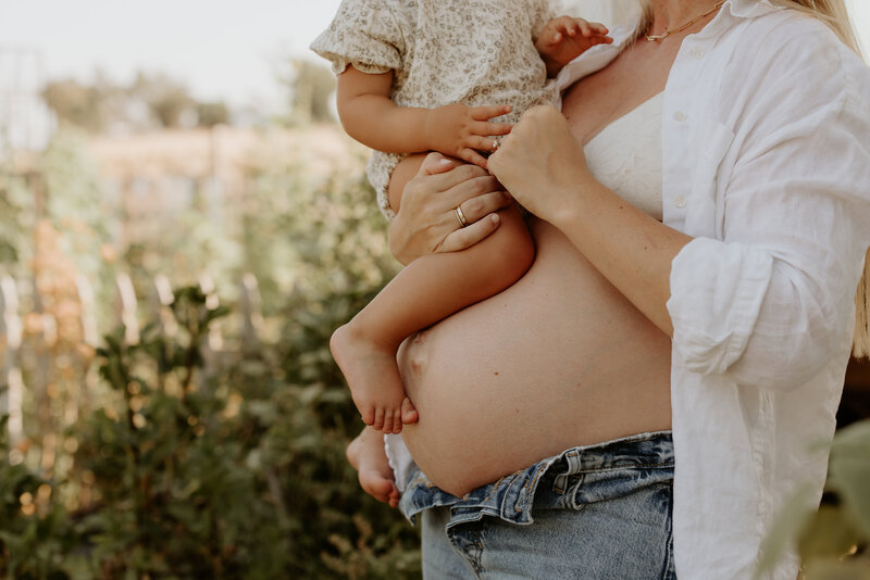 A woman holding a baby in a field at sunset.