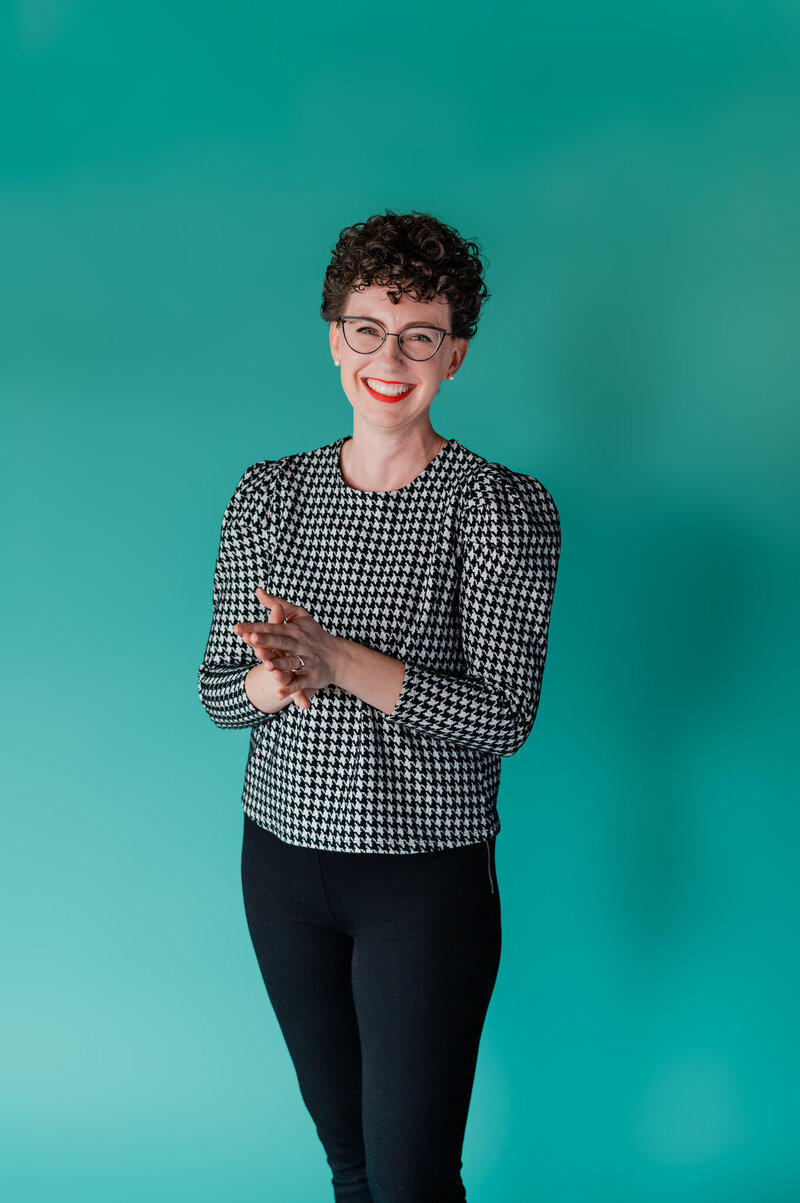 Wedding planner in black and white top standing in front of a teal background
