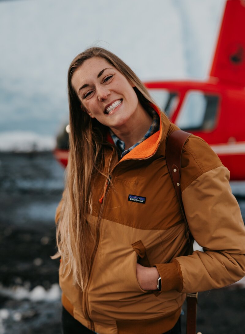 Portrait of Emmie Jackson, Anchorage-based Alaska wedding and elopement photographer, standing near a helicopter.