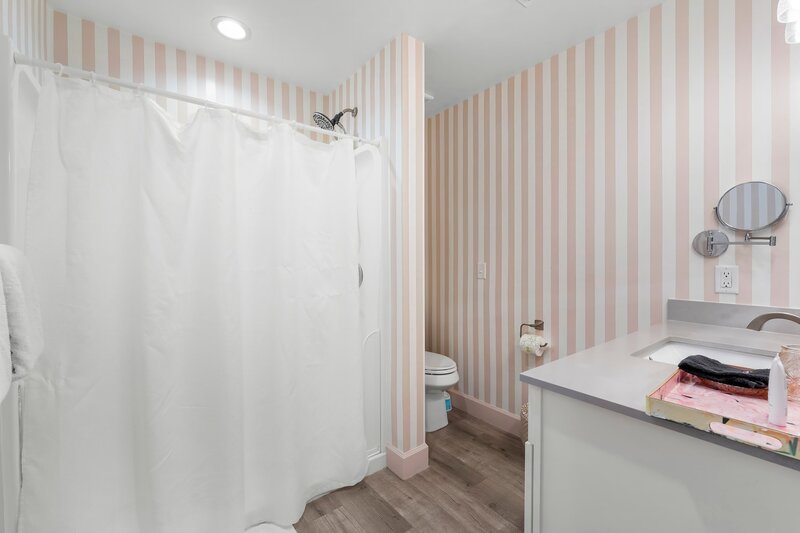 Striped pink and white bathroom featuring a walk-in shower with curtain, wood-style flooring, and modern vanity.