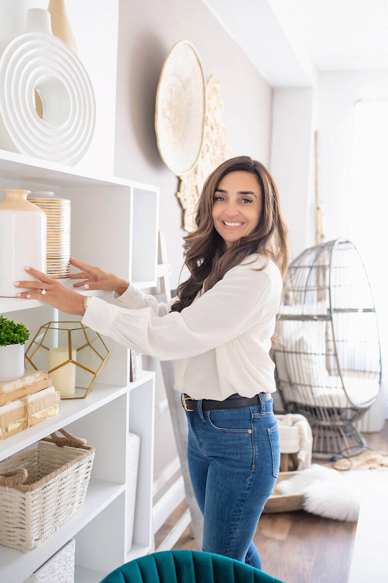 Shannon Brito, Home Stager smiling at the camera while fixing vases on a shelf