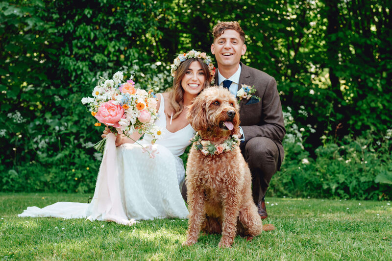 Bride and groom with a dog wearing a collar of flowers at Haybarn Dulus