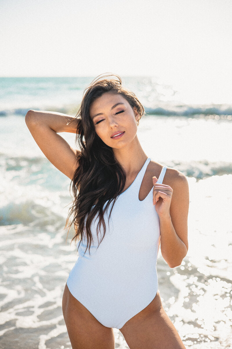 Model wears one piece white swimsuit on the beach for a swimwear photoshoot