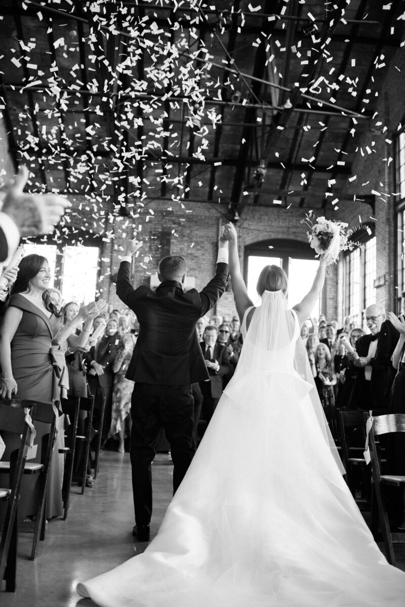 Bride and groom throw their hands in the air as confetti falls at their ceremony