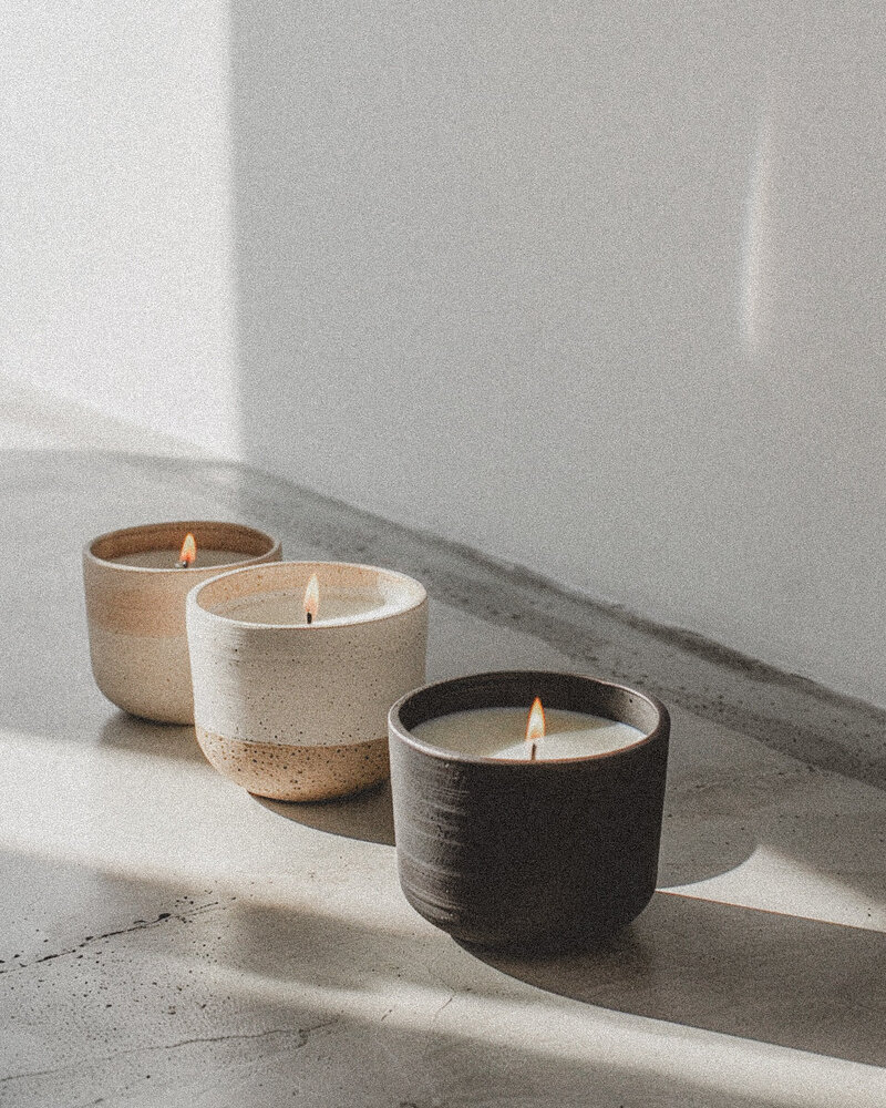 Three softly lit candles in ceramic holders casting warm light, symbolizing grounding, calm, and nervous system regulation in trauma therapy with Jessie Withers, California