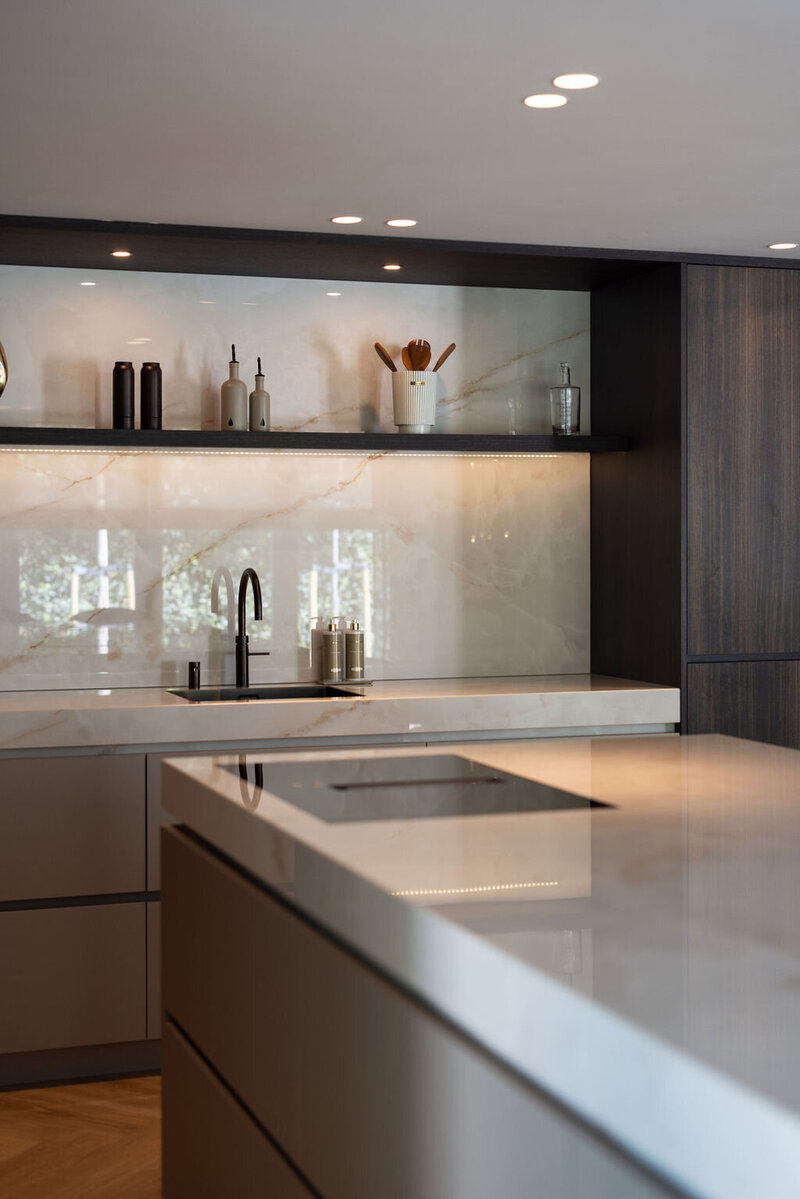 Maatwerk keuken met strakke lijnen, natuurstenen wand en donkere houttinten die perfect matchen met de rest van het interieur.