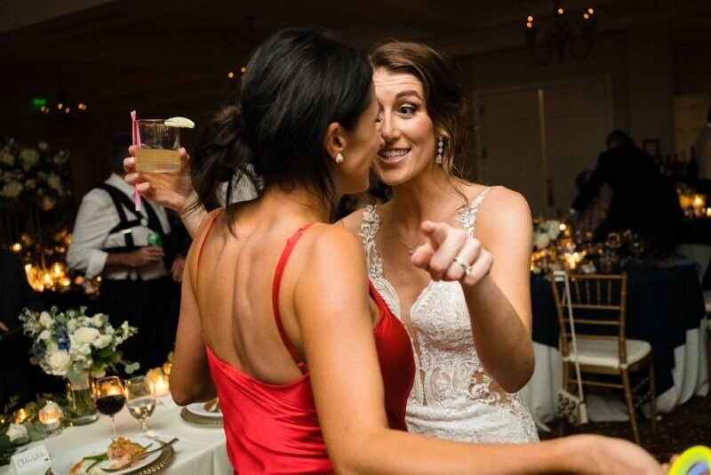 Two women dancing and laughing at a wedding reception one holding a drink and the other pointing playfully