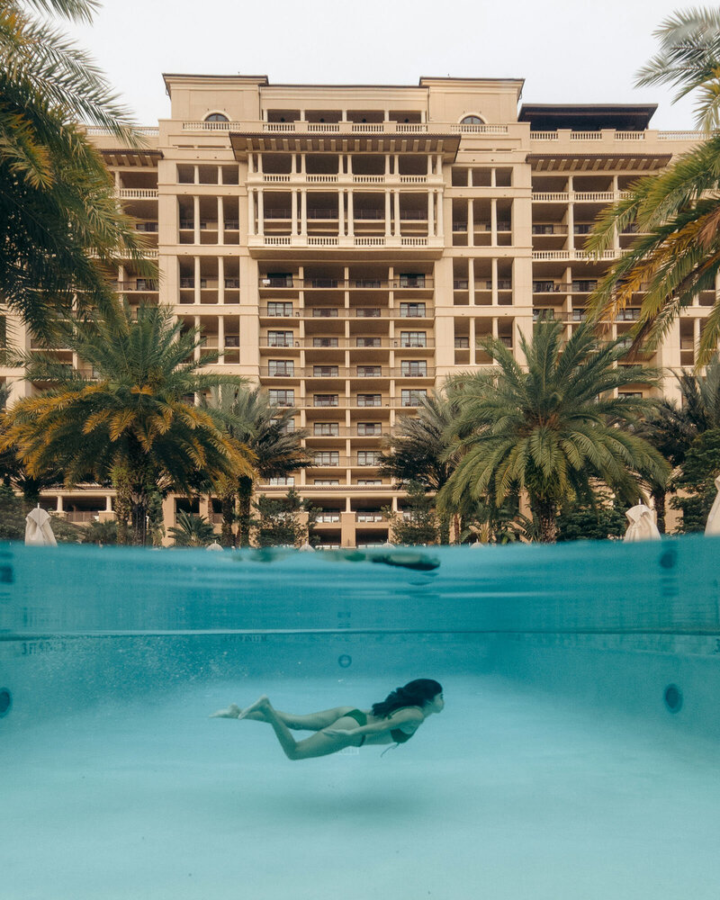 Woman swimming in a pool with a large building in the background