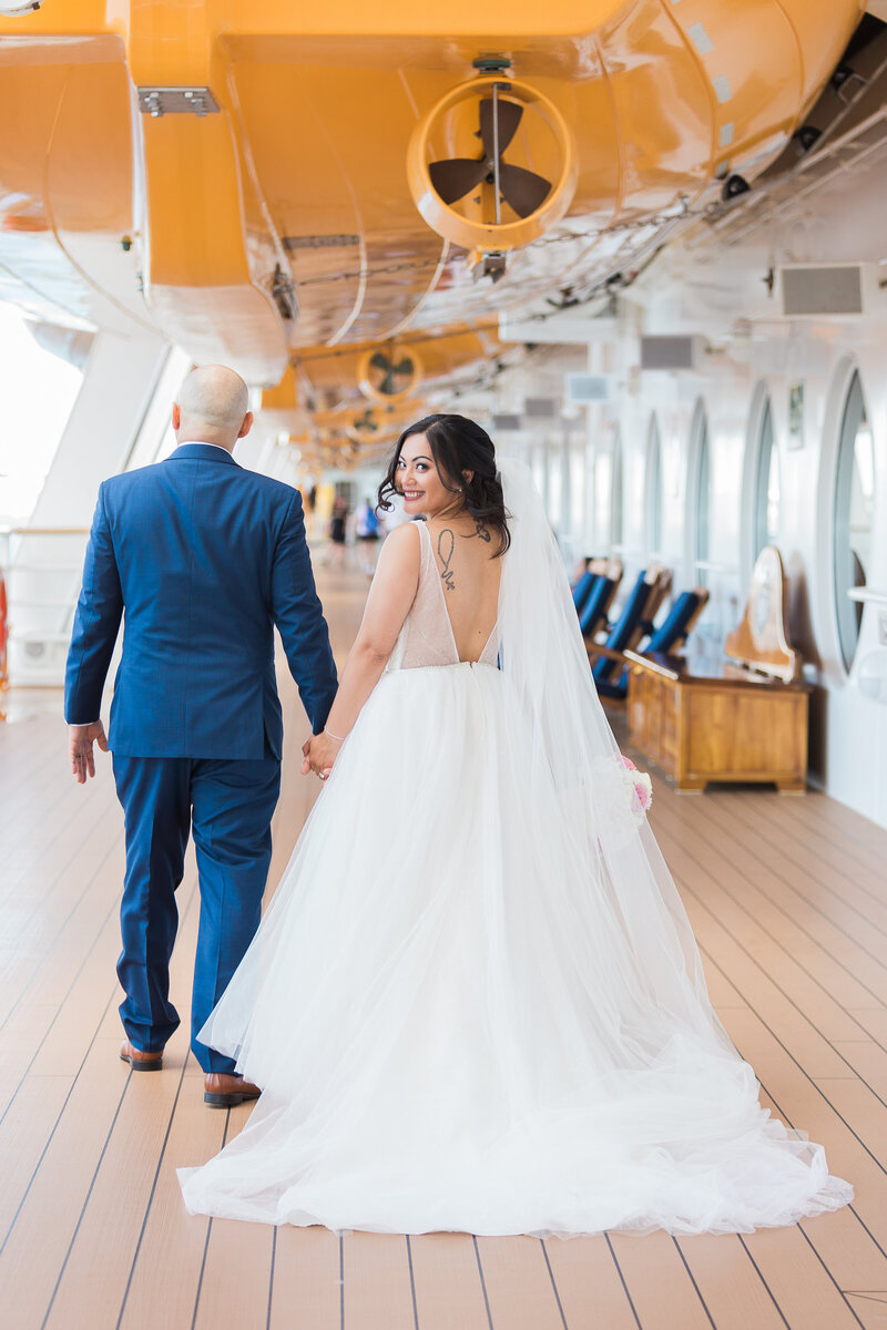 Bride smiling over shoulder as her and groom walk on Disney Cruise