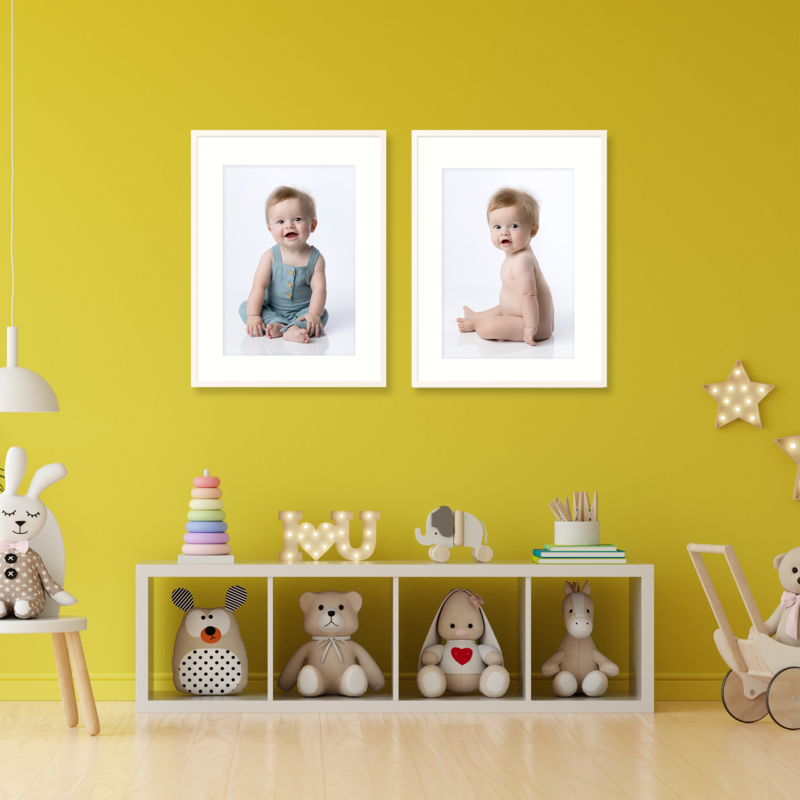 Wall display with framed baby portraits in a playroom with a yellow wall