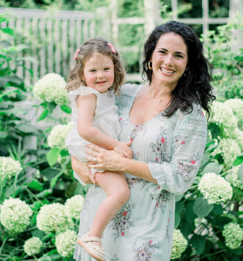 Caroline Busick smiling in Birmingham, Alabama botanical gardens holding her young daughter