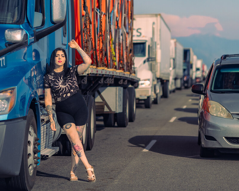 Editorial-style portrait photographed by Moonlit Photo on a Salt Lake City roadway, featuring a tattooed woman leaning against a bright blue semi-truck amid traffic. A bold, urban-inspired photoshoot showcasing creative, high-end portrait photography in Utah.