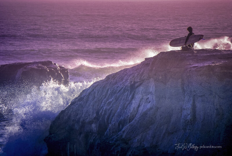 Surfer poised to scale cliffs to the challenge the surf below at Steamer Lane, Santa Cruz, CA.