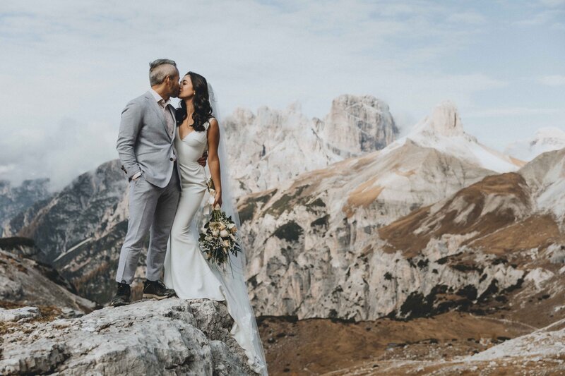 a couple in wedding attire kiss at sunrise in front of the Hintersee in the German Alps