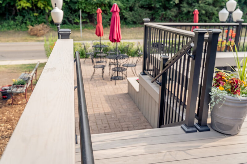 Light-colored drink rail on top of deck railing leading to a short staircase down to ground level. 