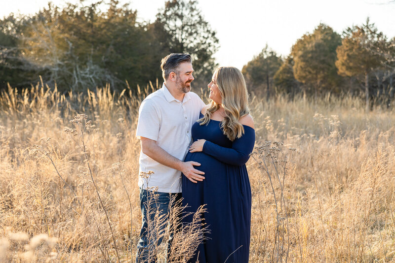 Expecting couple holding hands in a sunlit field during golden hour maternity session in Farmington Missouri.