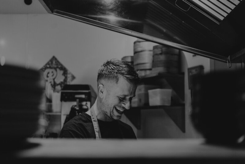 Chef smiling under a kitchen hood, caught candidly during service at Sael Birmingham restaurant.
