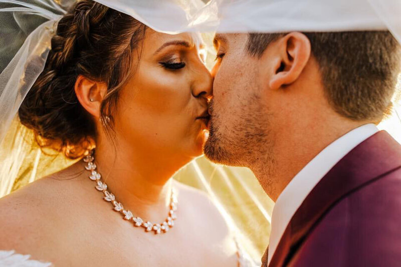 bride and groom kissing under her custom pearl bridal veil blusher during golden hour