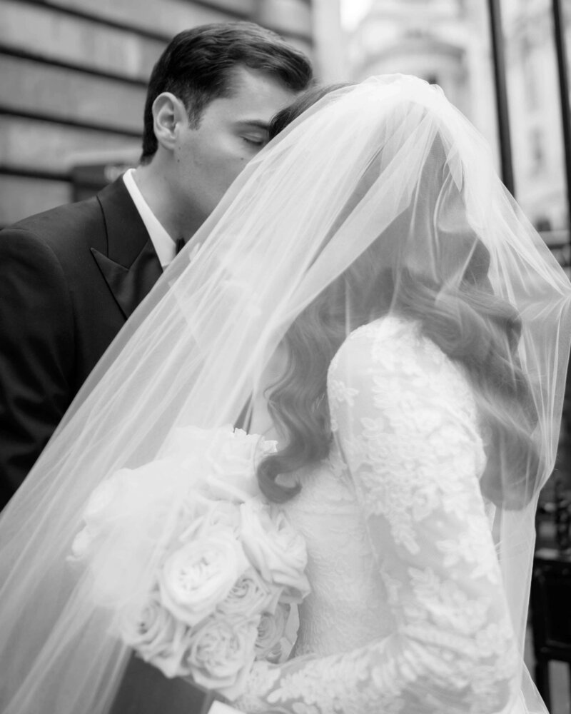 bride and groom kiss as the bride’s veil billows in the wind outside their bespoke event venue at the ned london