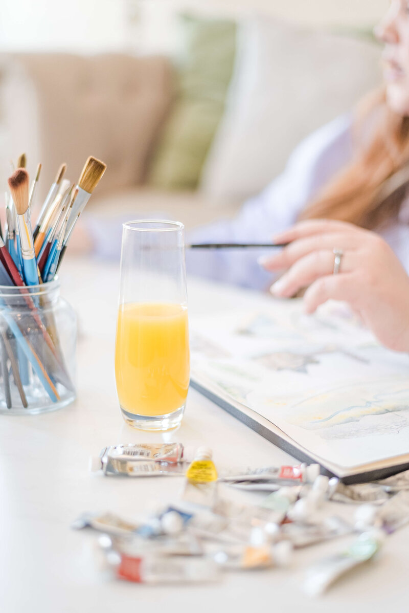 Designer surrounded by paint and paper, holding a paintbrush while creating wedding invitations