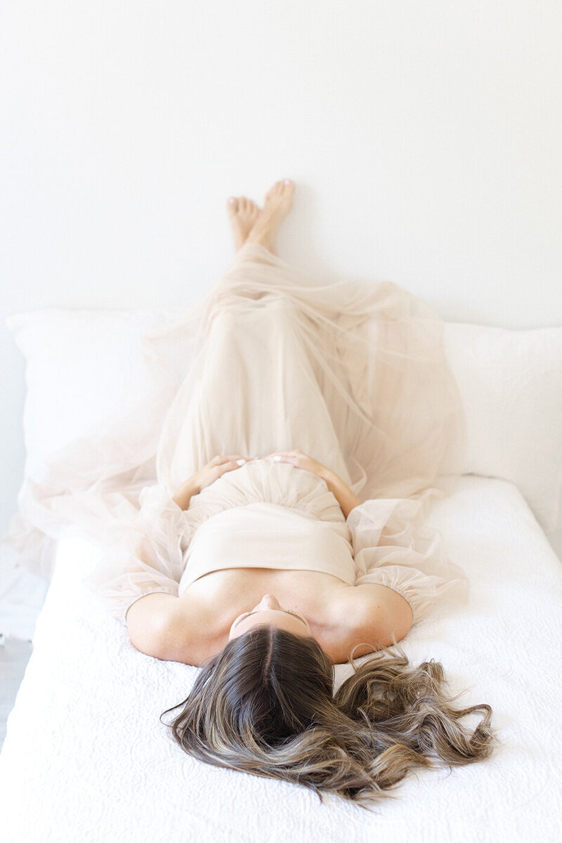 pregnant woman in pink tan tulle dress laying on bed feet up philadelphia newborn photographer