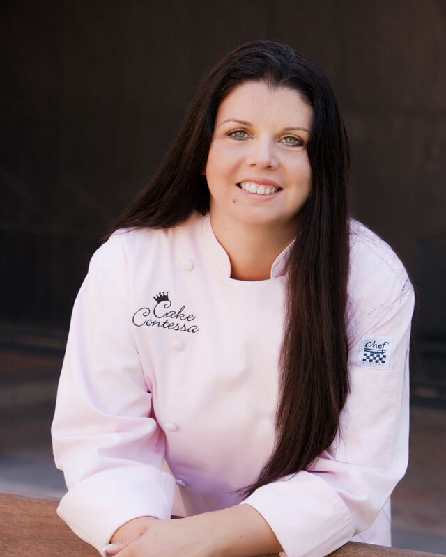 lanet miles headshot in a contess pink chef's apron smiling with brown hair and green eyes