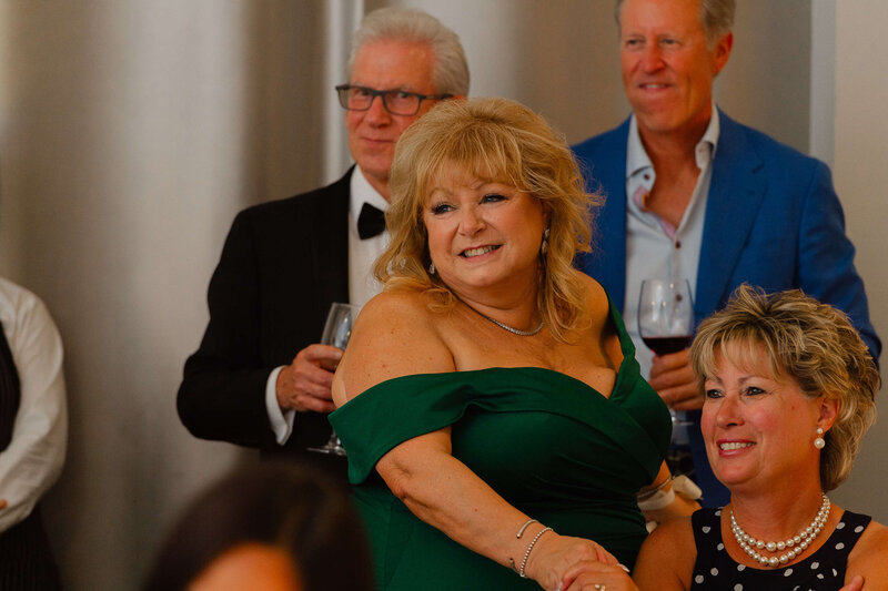 a mother of the groom in a green dress looks fondly at her son during his speech.  Captured by Ottawa wedding photographer JEMMAN Photography