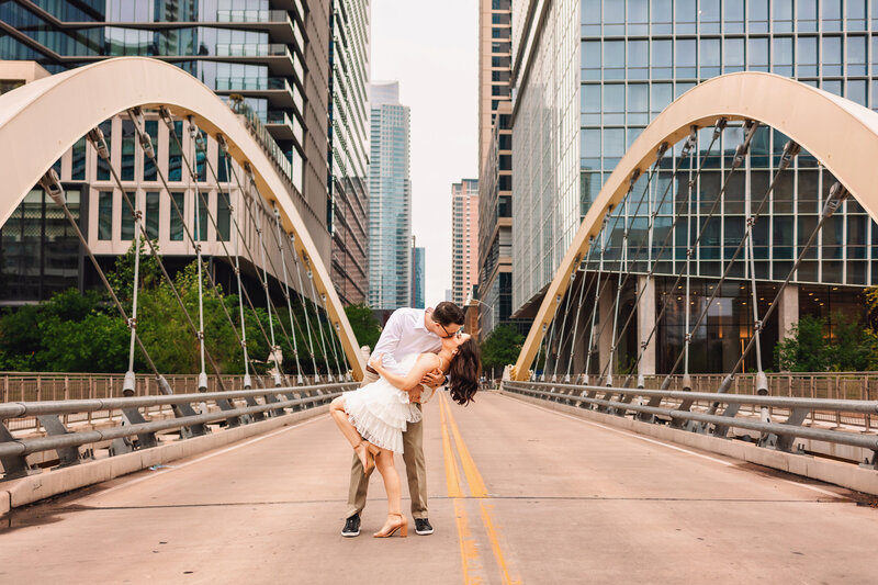 future groom dips his soon-to-be bride at their sunrise summer engagement photo session on the butterfly bridge in downtown austin