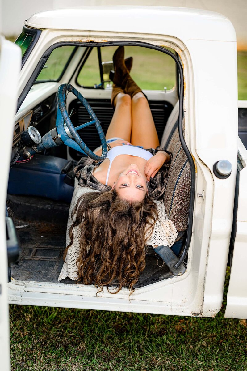 graduate portrait of senior girl wearing white tank and flannel with jean shorts laying in a truck seat