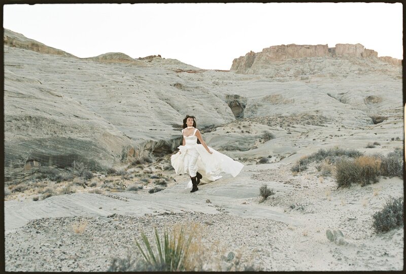 Bride running through Arizona desert in luxury wedding dress and boots | Artful candid moment by Arizona editorial film wedding photographer Tess Gearhart