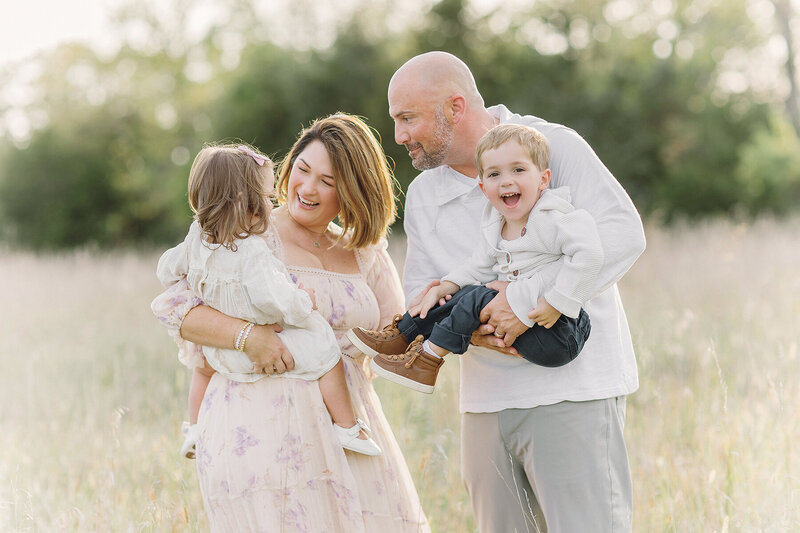 Mom, Dad, and two kids laughing in a field. Family having fun. Kansas City photography by Jeanna Hayes