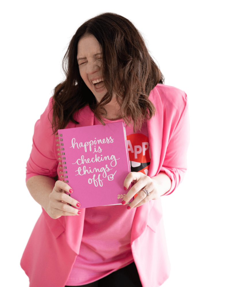 Emily smiling and closing her eyes while holding a pink notebook that says "happiness is checking things off."