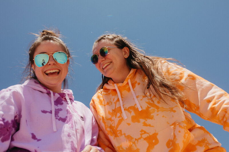 two girls laugh under a blue sky