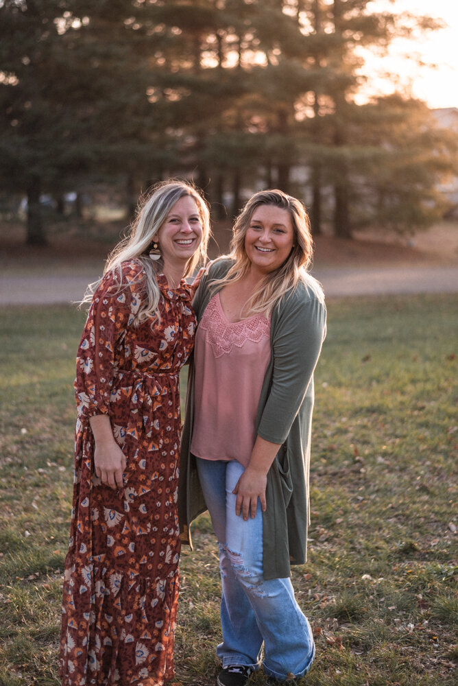 Sister in law photography team stand side by side wearing casual maxi dress and jeans with nice pink top and cardigan in wooded area photo by juniper and oak photo