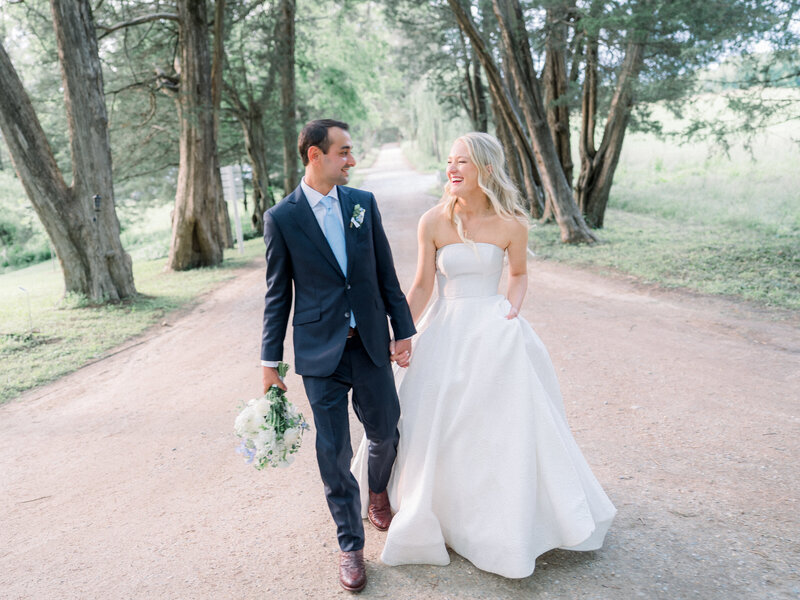 Bride and groom walking hand-in-hand down a colonial-style path in Yorktown, Virginia, during their wedding, coordinated by Sweet Caroline Events. Photo by Marshall Arts Photography.