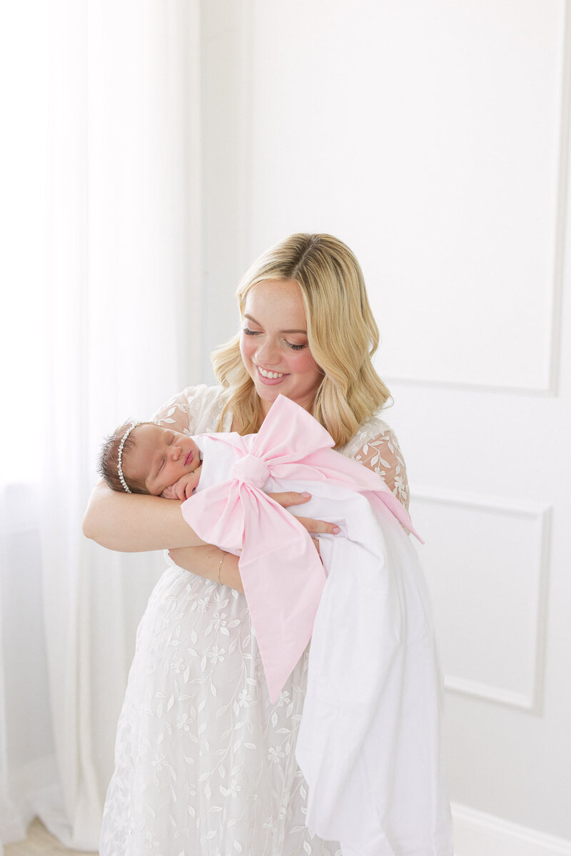 Portrait of newborn baby girl swaddled in a Beaufort Bonnet bow swaddle while being held by her mom taken by newborn photographer Missy Marshall