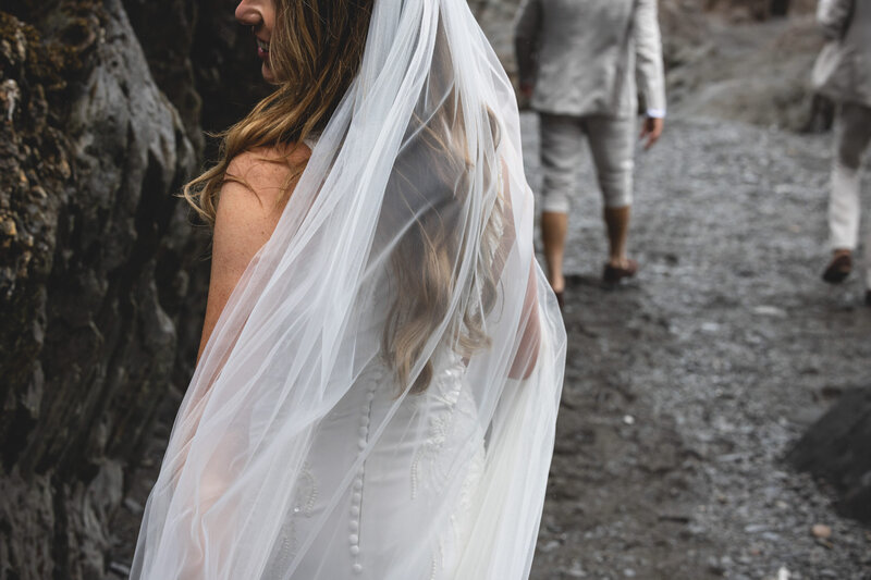 Bride following Groom on wet wedding at Tunnels Beaches in Devon