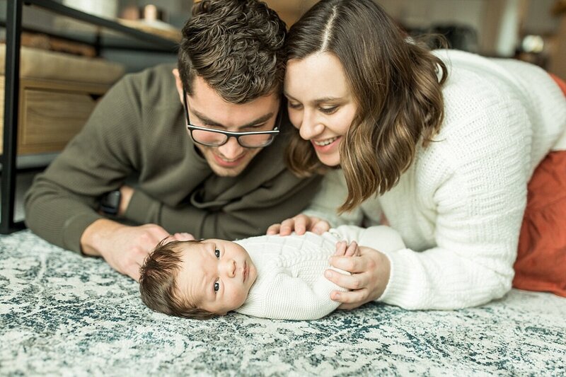 A mom and dad smiling at their baby who is lying on the floor