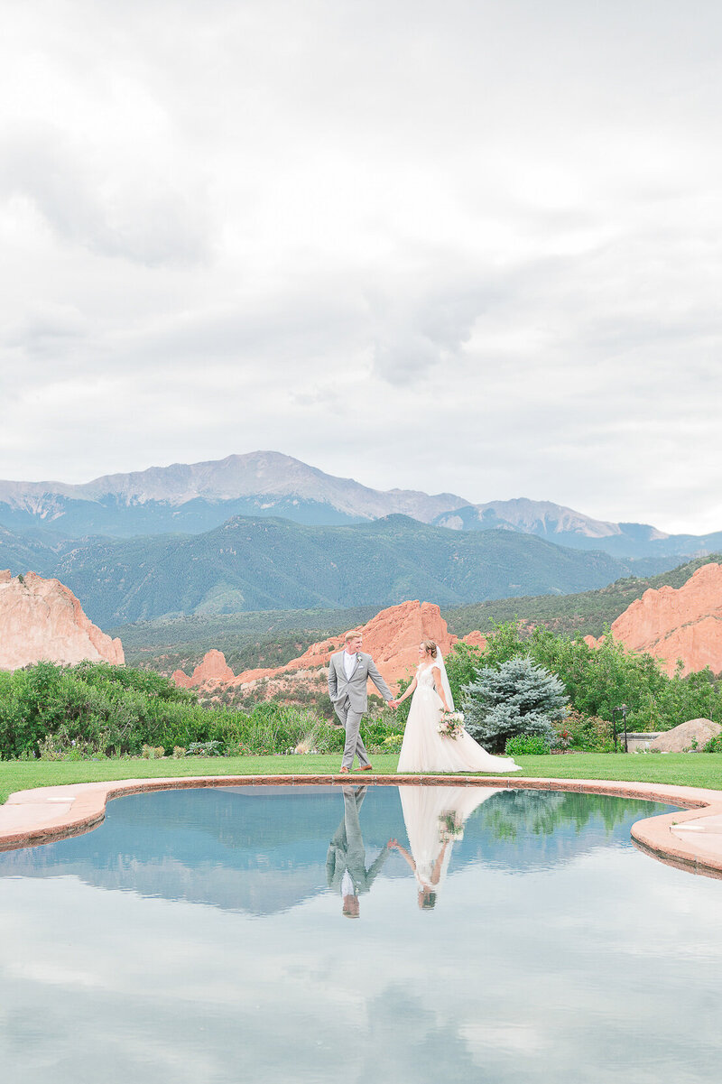 Groom leading bride by a reflection pool with Pikes Peak in the background.