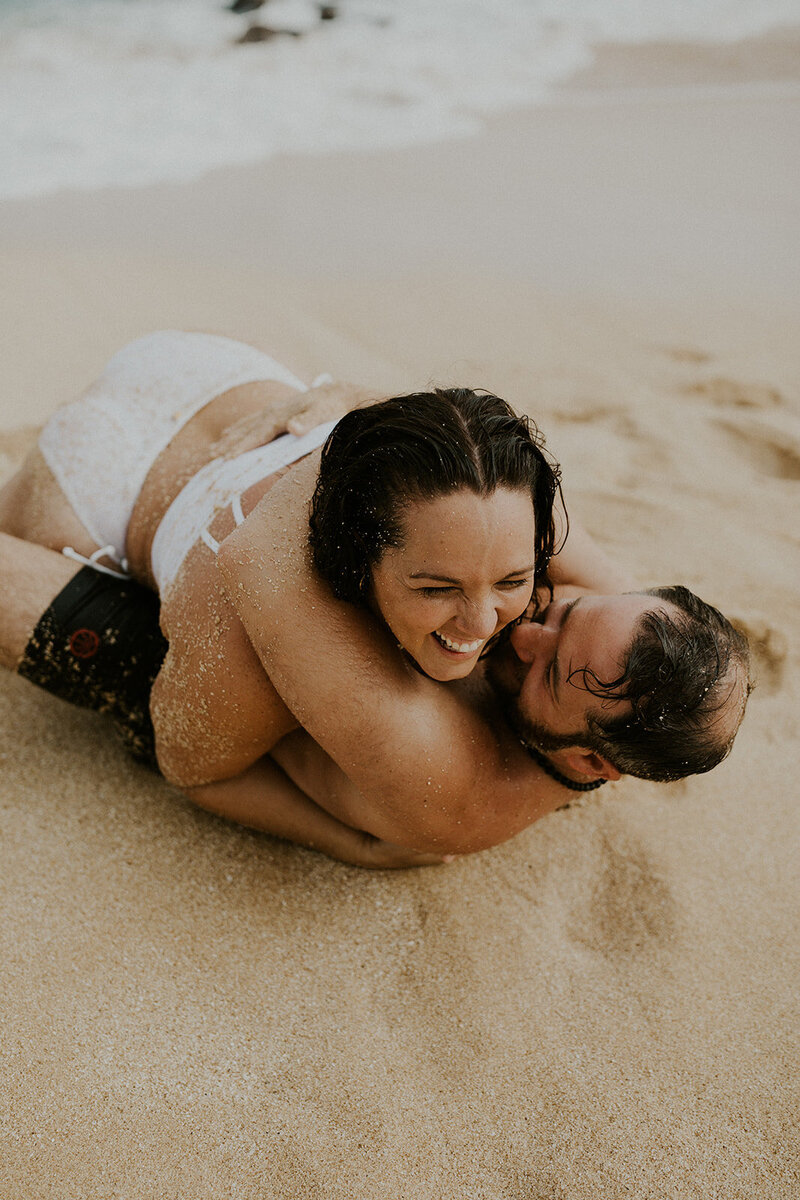 Ryan and Jess Collins laughing and hugging on a beach