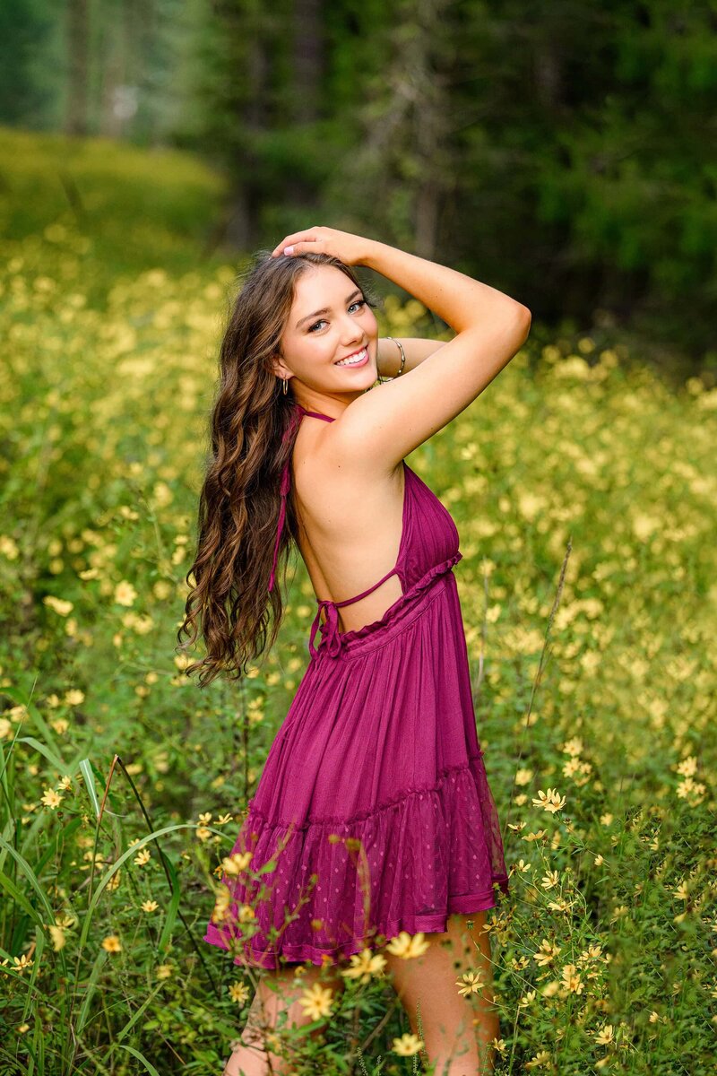 waxhaw grad has her hands in her hair as she stands in a field of yellow flowers in a purple dress
