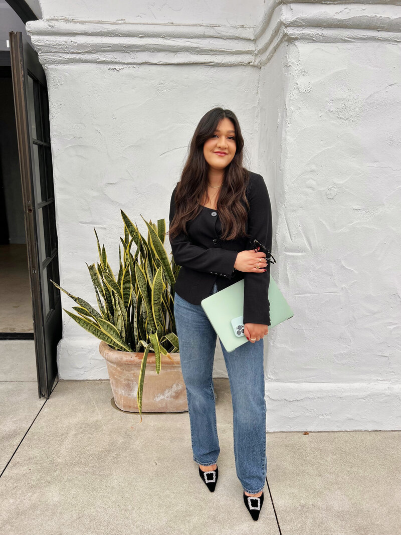 latina web designer standing holding laptop and iphone