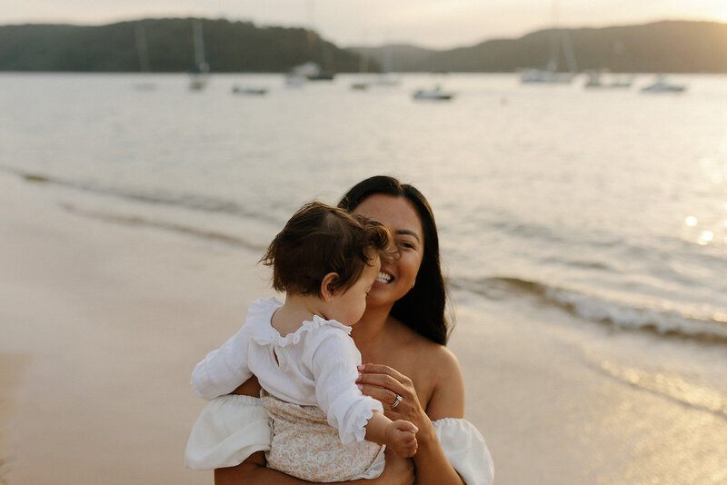 Mother smiling and holding her baby at the beach.