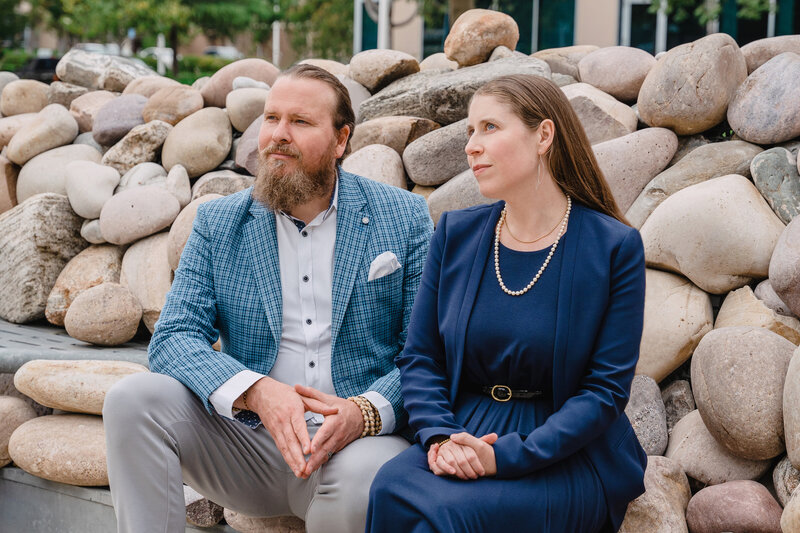 Rebecca and Jarrett sitting in front of rocks wearing a blue blazer and a blue dress