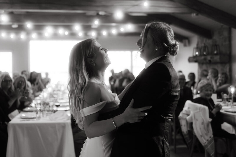 Two brides laughing while dancing together at their wedding reception in black and white