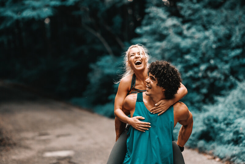 Young woman laughing while getting a piggy back ride from smiling man