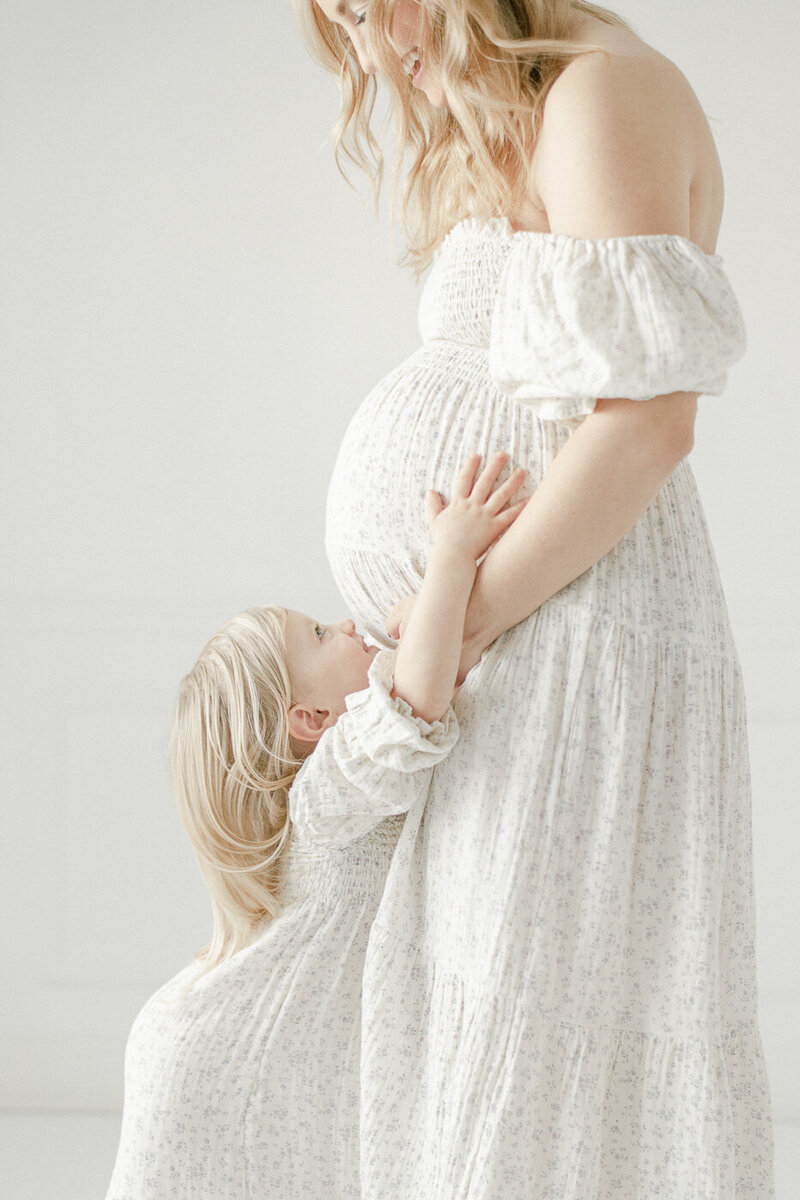 a little girl reaches up to hug her moms pregnant stomach