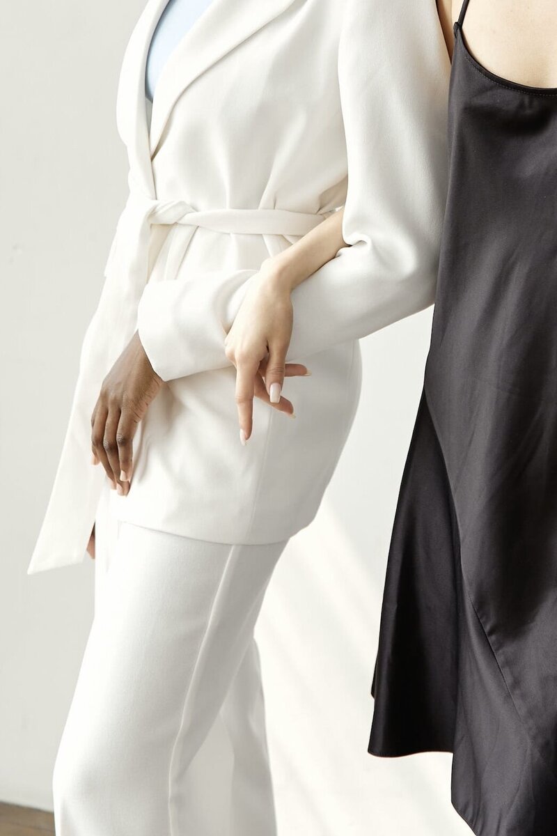 A professional in a white suit, their arm intertwined with another professional in a black dress